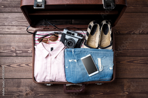 Open suitcase with casual female clothes on wooden table