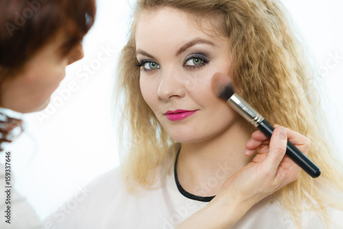 Makeup artist applying with brush rouge on female check