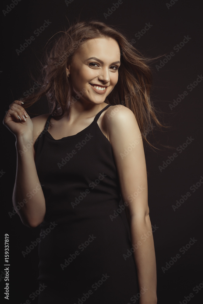 Smiling brunette model in black dress with curly hair in motion
