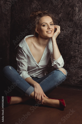 Happy young model in shirt and jeans sitting on the floor
