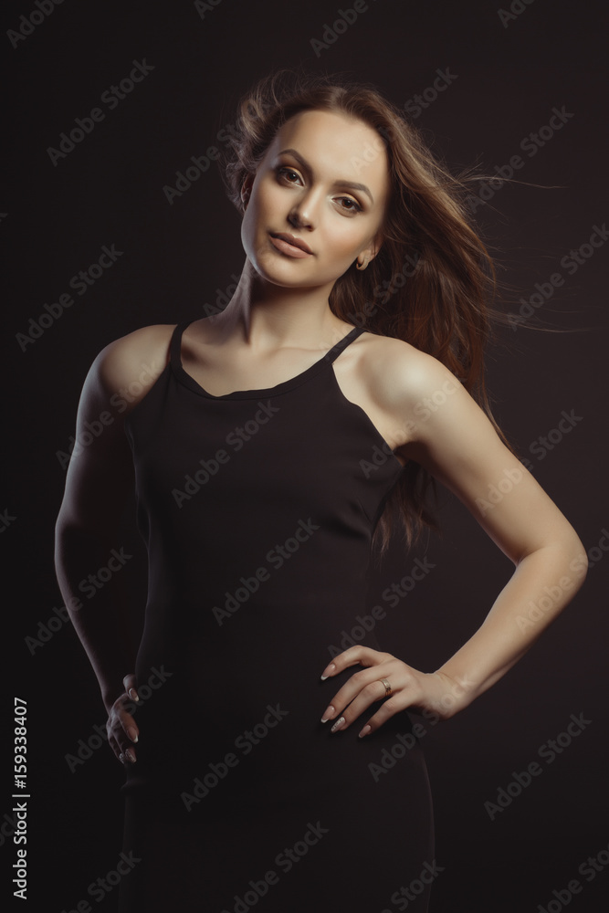 Beautiful brunette model in black dress with fluttering hair with wind
