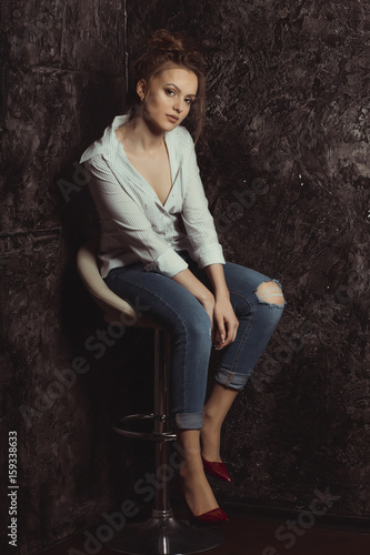 Attractive young model sitting on a chair  in striped and torn jeans