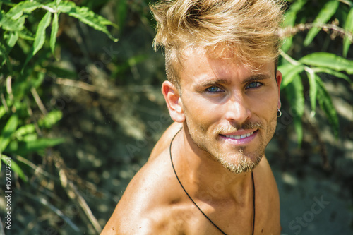 Head and shoulders shot of shirtless blond young man seen from above, looking at camera with a smile