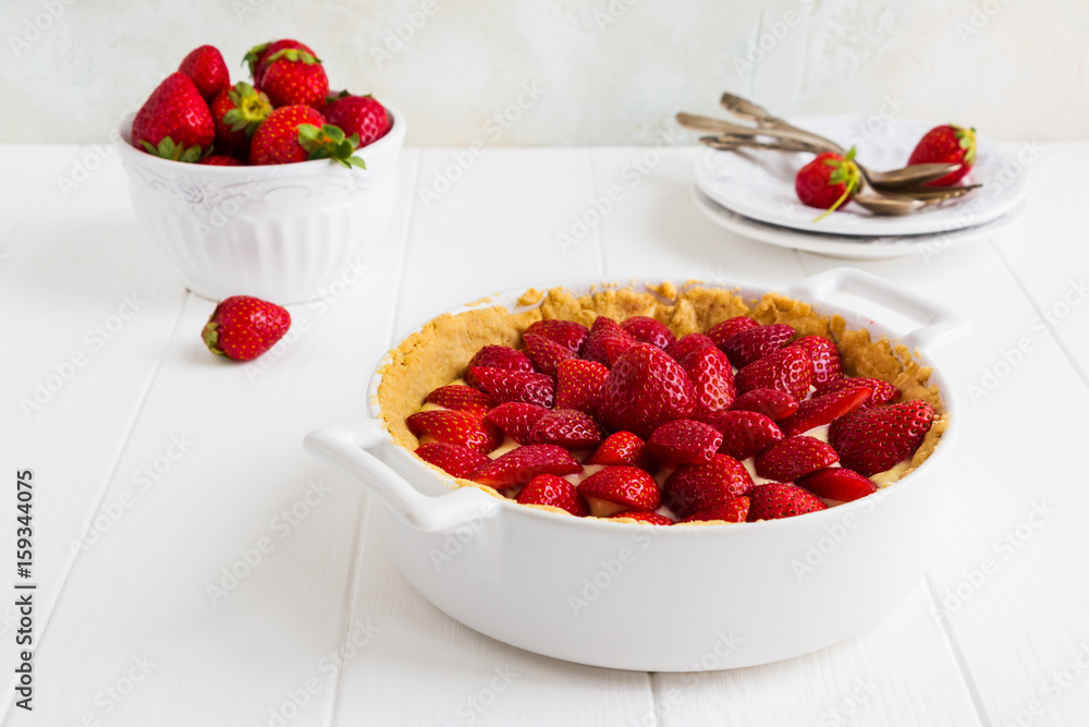 Homemade French tart with strawberries in a custard. White pan, fresh berries and vintage plates on the wooden table.