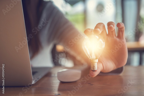 New ideas with innovation and creativity concept, Young women hand holding light bulb while using on laptop. photo