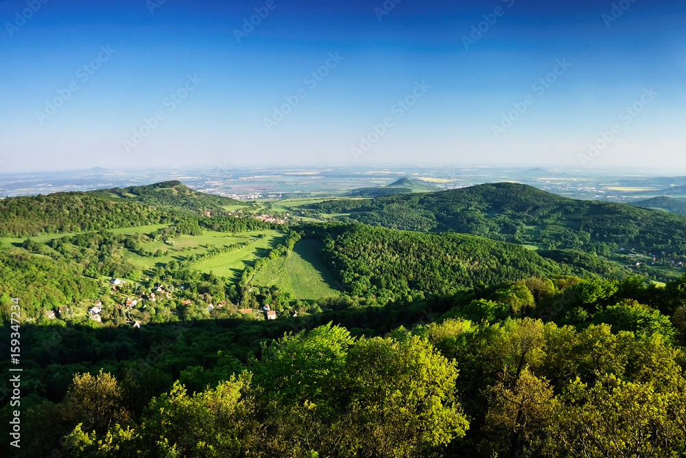 Ceske Stredohori tourist area with hill Kamyk and Litomerice city on horizont and Kundratice village in foreground in spring evening czech landscape during sunset