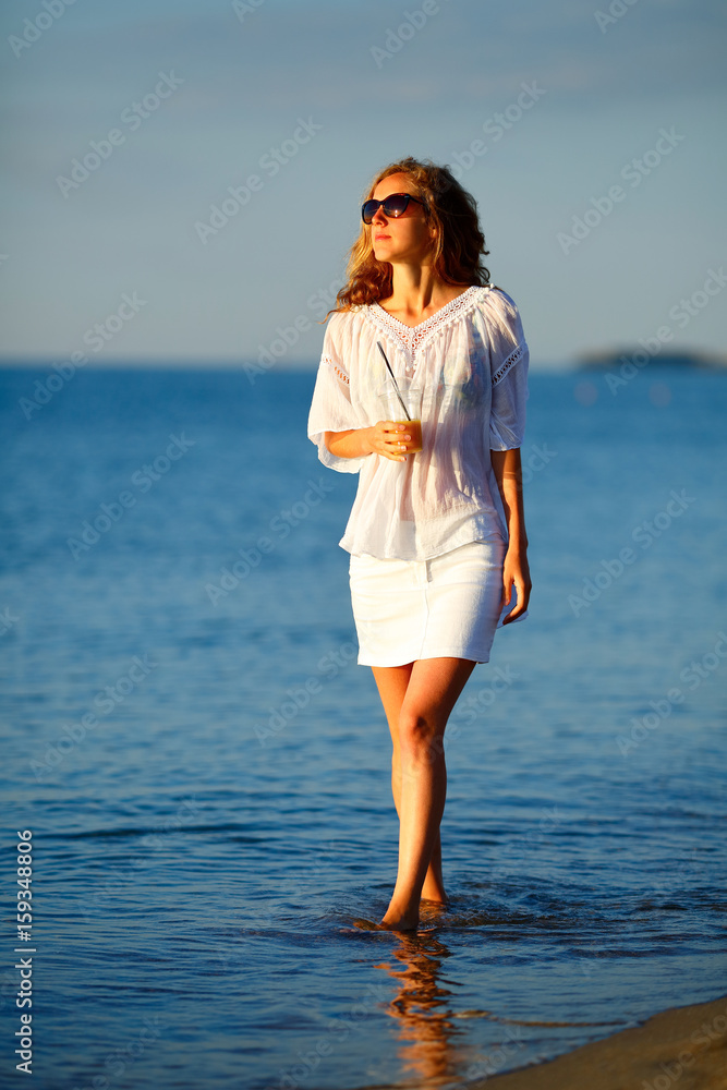 Beautiful woman with orange juice in hand in white clothes on the beach Beautiful woman with orange juice in hand in white clothes on the beach