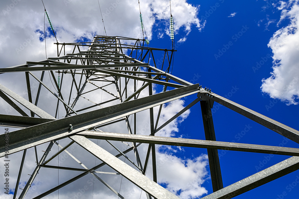 The electricity transmission pylon in daytime outdoors. Electricity tower standard overhead power line transmission tower on the background blue sky and white cloud.