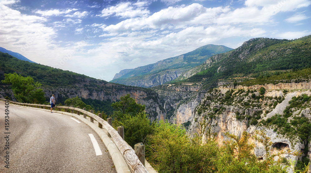 A young man stands on the edge of a mountain road and admires the panorama of the mountains.The man admires the view of the mountains and the Verdon gorge from the mountain road.Verdon Canyon, Verdon 