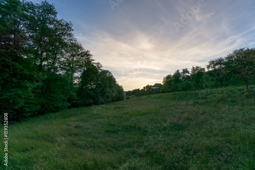 Evening atmosphere on green meadows with colorful sky and trees