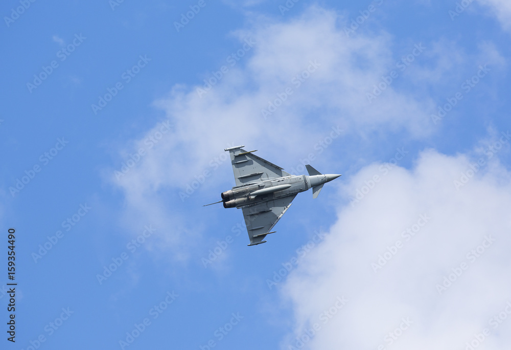 Modern jet fighter flying high against the blue sky with some clouds. Modern jet fighter flying high against the blue sky with some clouds.