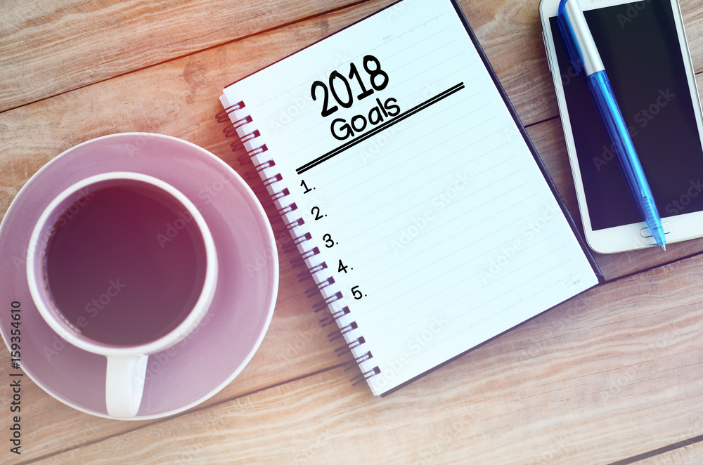 2018 goals list on note pad, wood table with coffee, pen and smart phone retro styled. 2018 goals list on note pad, wood table with coffee, pen and smart phone retro styled.