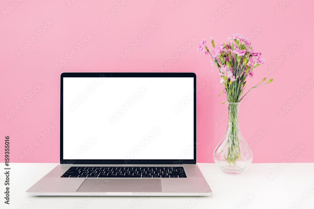 Laptop with white blank screen and flowers in vase on table on pink background. mock up Laptop with white blank screen and flowers in vase on table on pink background. mock up