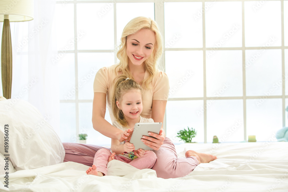 Young mother and daughter morning on bed indoors Young mother and daughter morning on bed indoors