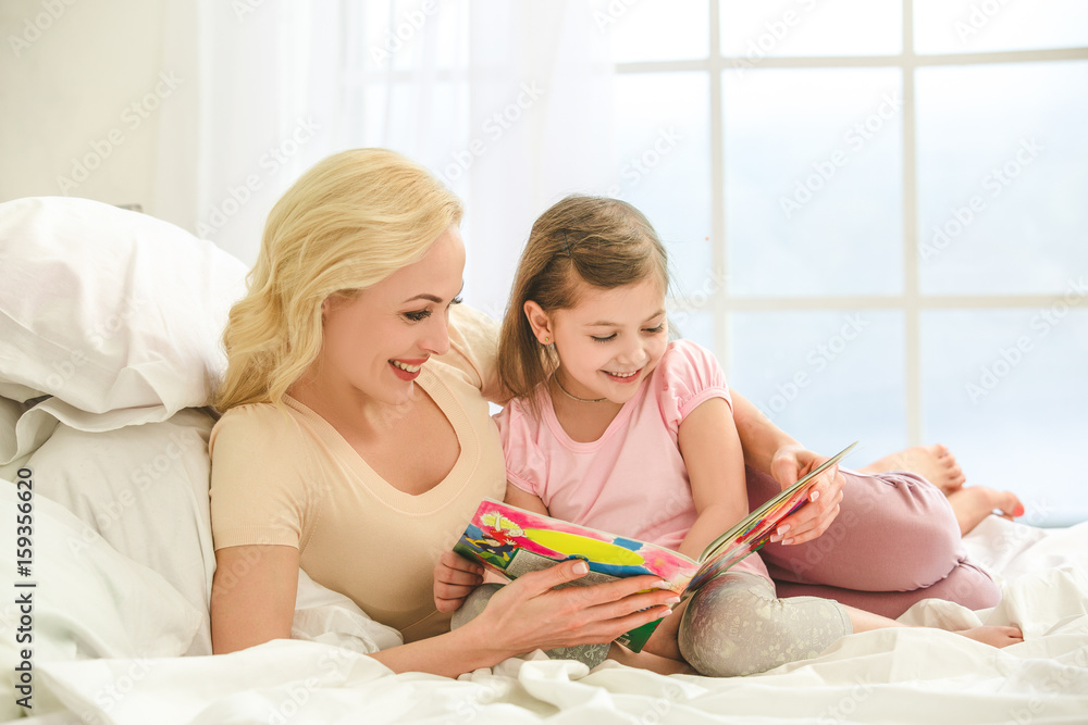 Young mother and daughter morning on bed indoors Young mother and daughter morning on bed indoors