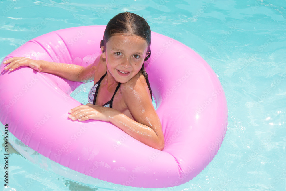 pretty young girl child in pool with pink buoy in pool at garden house
