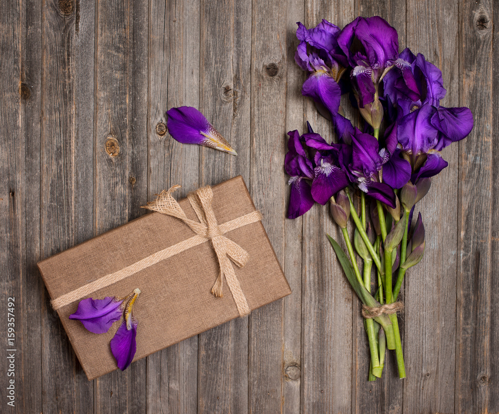 Purple iris flowers bouquet and gift box on weathered wooden background. Holiday and present concept.