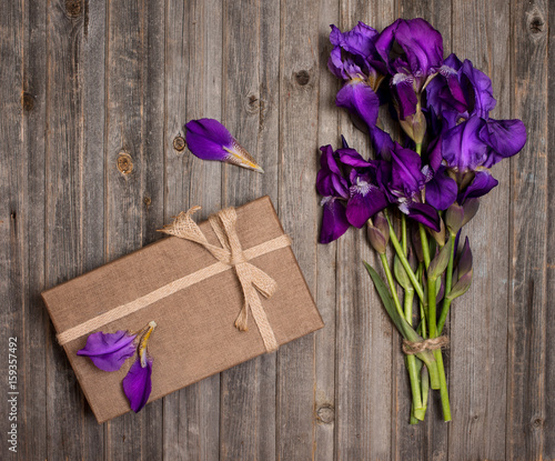 Fototapeta Naklejka Na Ścianę i Meble -  Purple iris flowers bouquet and gift box on weathered wooden background. Holiday and present concept.