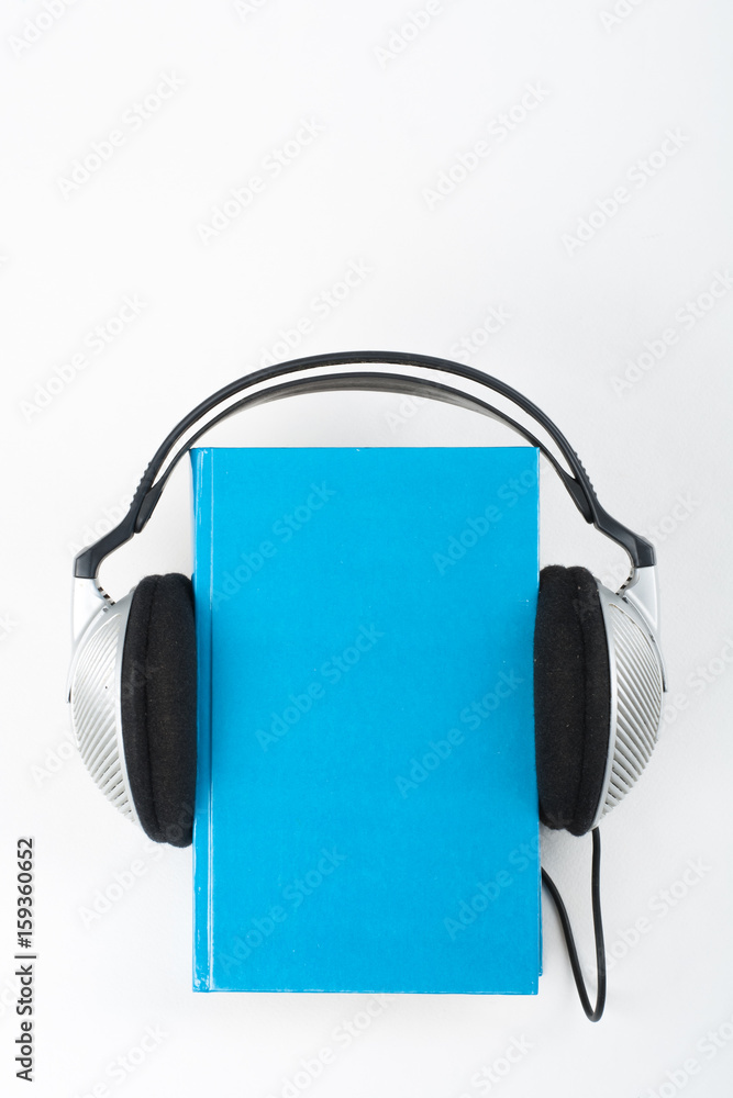 Audiobook on white background. Headphones put over blue hardback book, empty cover, copy space for ad text. Distance education, e-learning concept. Audiobook on white background. Headphones put over blue hardback book, empty cover, copy space for ad text. Distance education, e-learning concept.