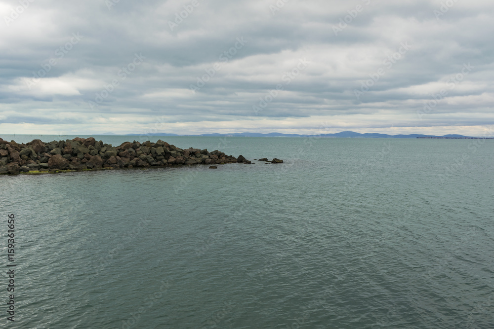 Cloudy day at sea with rocks and calm water Cloudy day at sea with rocks and calm water