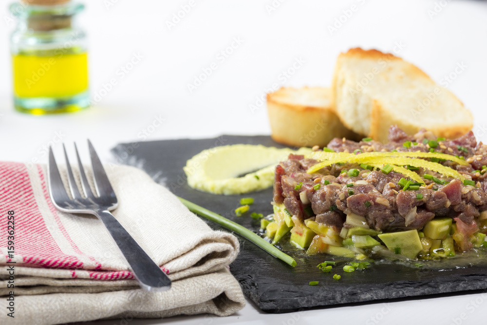 Bluefin tuna tartare on a black slate plate with avocado, served with grilled bread.