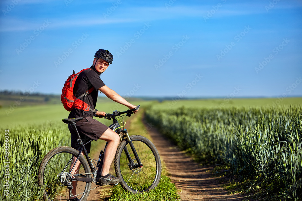 Young attractive cyclist standing up with mountain bicyclist in the summer green field.