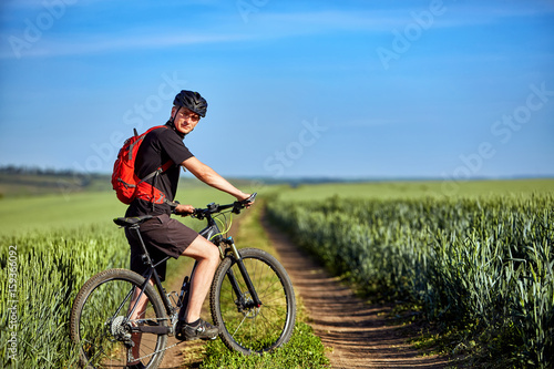 Young attractive cyclist standing up with mountain bicyclist in the summer green field.