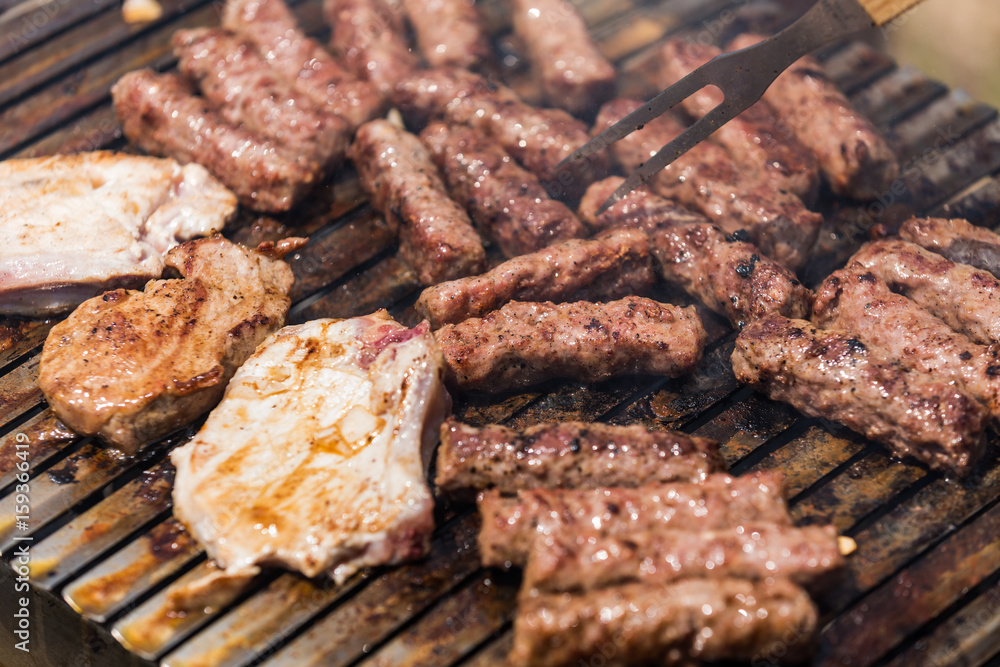 Grilling minced meat on a barbecue grill with coal; outdoors picnic with minced pork meat rolls (also known as mici, mititei, cevapi or cevapcici) Grilling minced meat on a barbecue grill with coal; outdoors picnic with minced pork meat rolls (also known as mici, mititei, cevapi or cevapcici)
