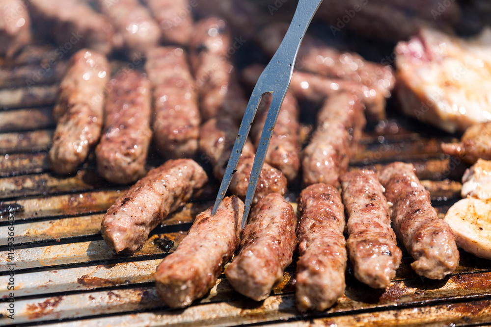 Grilling minced meat on a barbecue grill with coal; outdoors picnic with minced pork meat rolls (also known as mici,   mititei, cevapi or cevapcici)