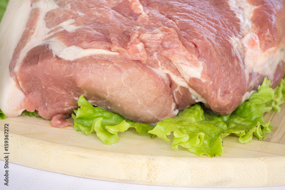 Raw cervical carbonate of pork on cutting board with leaves of green salad, isolated on white background Raw cervical carbonate of pork on cutting board with leaves of green salad, isolated on white background