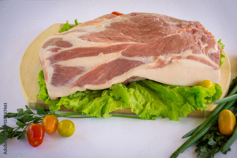 Raw cervical carbonate of pork on cutting board with leaves of green salad, vegetables, tomatoes, parsley and onion, isolated on white background Raw cervical carbonate of pork on cutting board with leaves of green salad, vegetables, tomatoes, parsley and onion, isolated on white background