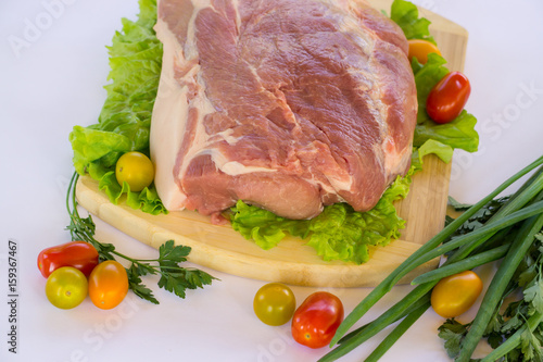 Raw cervical carbonate of pork on cutting board with leaves of green salad, vegetables, tomatoes, parsley and onion, isolated on white background