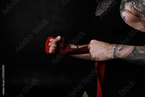 Fighting concept. Brutal tattooed hands with red bandage ready for a battle. Strong man cropped portrait. Background for kickbox sport. Copy space for advertising.