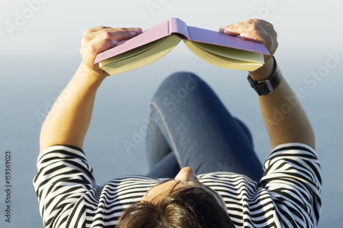 woman reading book near to sea