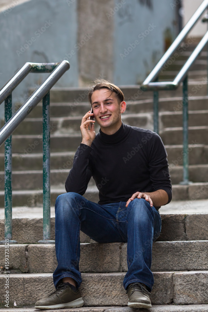 Young man talking on mobile while sitting on the stone stairs in the old town. Young man talking on mobile while sitting on the stone stairs in the old town.