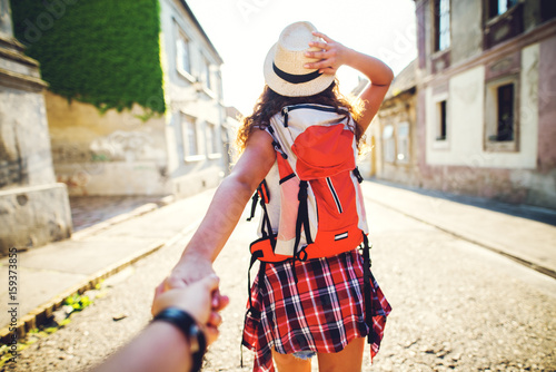 Beautiful girlfriend with red backpack holding boyfriend's hand.