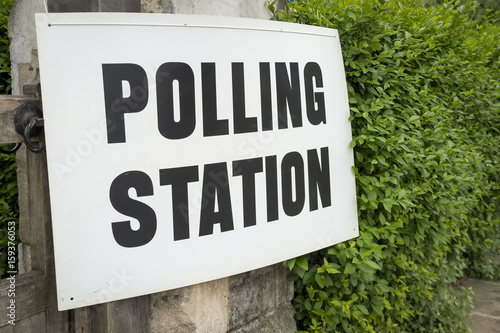 British election polling station sign hanging on gate post next to a green hedge in the UK photo