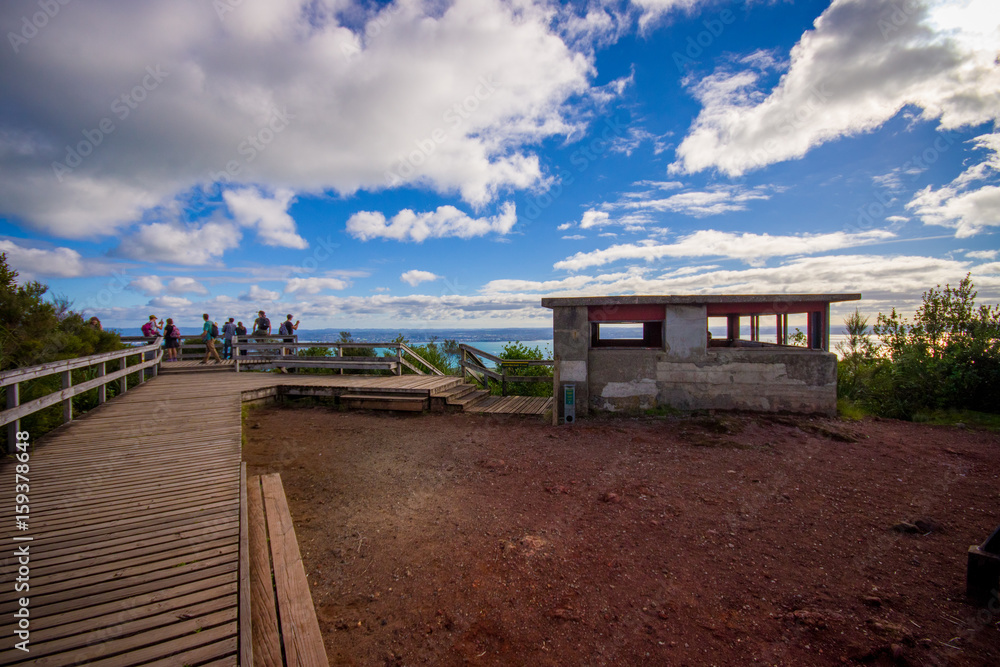 People enjoying the beautiful view from top in the mountain in Rangitoto Island wlaking in wooden paths, New Zealand in a sunny day