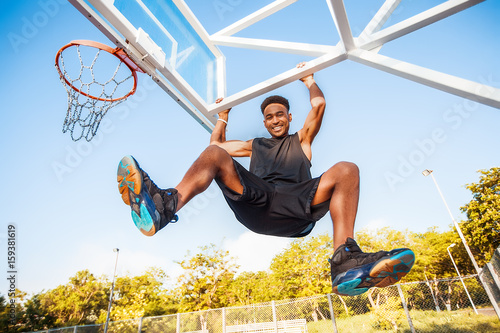Basketball player hangs on the rim.attractive,laugh,sport games,street ball,black,sport outfit,casual wear,black clothes