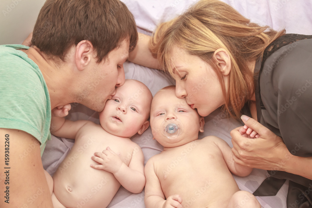 indoor portrait of young happy smiling mother and father with twin babies at home