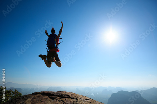 cheering woman backpacker jumping on sunrise mountain top