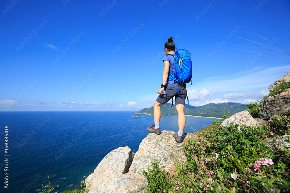 successful woman backpacker enjoy the view on seaside mountain rock