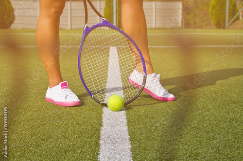 Good legs stands with racket on court at sunny summer day