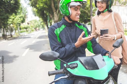 woman standing on sidewalk ordering a commercial motorcycle taxi driver by phone