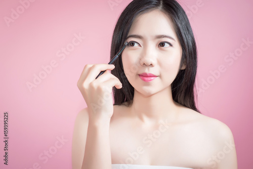 Long hair asian young beautiful woman applying cosmetic powder brush on smooth face isolated over pink background. natural makeup, SPA therapy, skincare, cosmetology and plastic surgery concept.