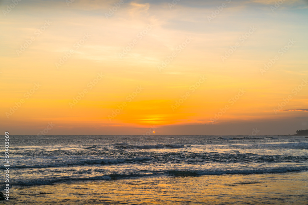 Sunset beach in Bali - Echo beach. Waves, tide and magic sea landscape view with a beautiful evening sky. Indonesia, Ocean. Orange beach pattern. Surfing Waves on the Tropical Beach. Panoramic Sunset