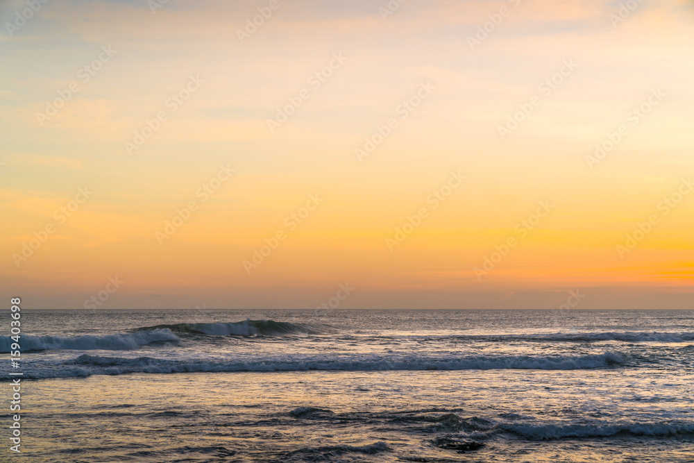 Sunset beach in Bali - Echo Beach. Waves, tide and magic sea landscape view with a beautiful evening sky. Indian Ocean. Orange beach pattern. Surfing Waves on the Tropical Beach. Panoramic Sunset