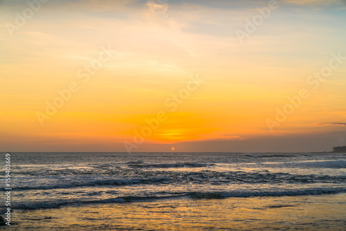 Sunset beach in Bali - Echo beach. Waves, tide and magic sea landscape view with a beautiful evening sky. Indonesia, Ocean. Orange beach pattern. Surfing Waves on the Tropical Beach. Panoramic Sunset