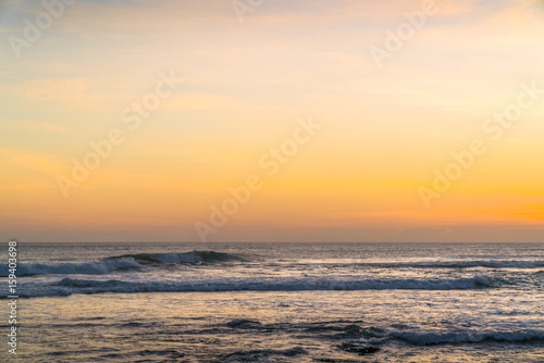 Sunset beach in Bali - Echo Beach. Waves  tide and magic sea landscape view with a beautiful evening sky. Indian Ocean. Orange beach pattern. Surfing Waves on the Tropical Beach. Panoramic Sunset