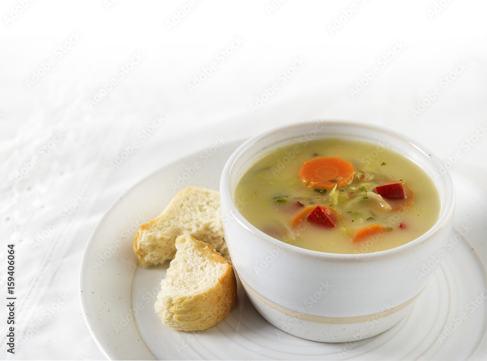 Vegetable cream soup with carrot, red pepper and leek in a bright bowl and bread on a plate, white table cloth, background with copy space fades to white Vegetable cream soup with carrot, red pepper and leek in a bright bowl and bread on a plate, white table cloth, background with copy space fades to white